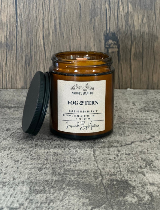 Earthy and crisp fog & fern beeswax candle in an amber glass jar, inspired by nature's misty morning